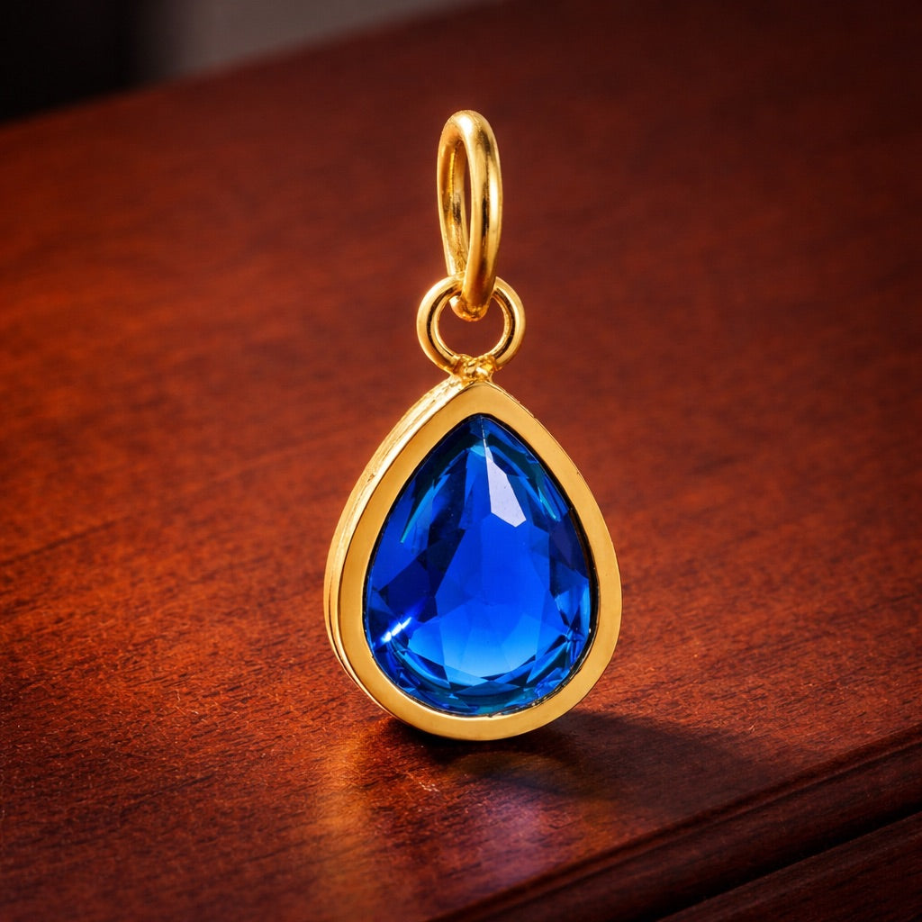 Gold pendant with a blue teardrop-shaped gemstone on a wooden surface