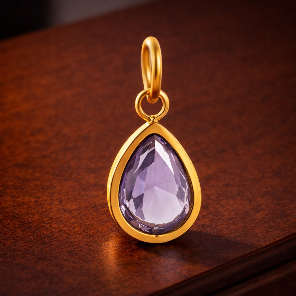 Gold pendant with a purple teardrop-shaped gemstone on a wooden surface