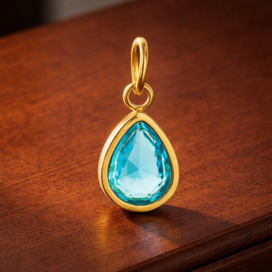 Gold pendant with a blue teardrop-shaped gemstone on a wooden surface