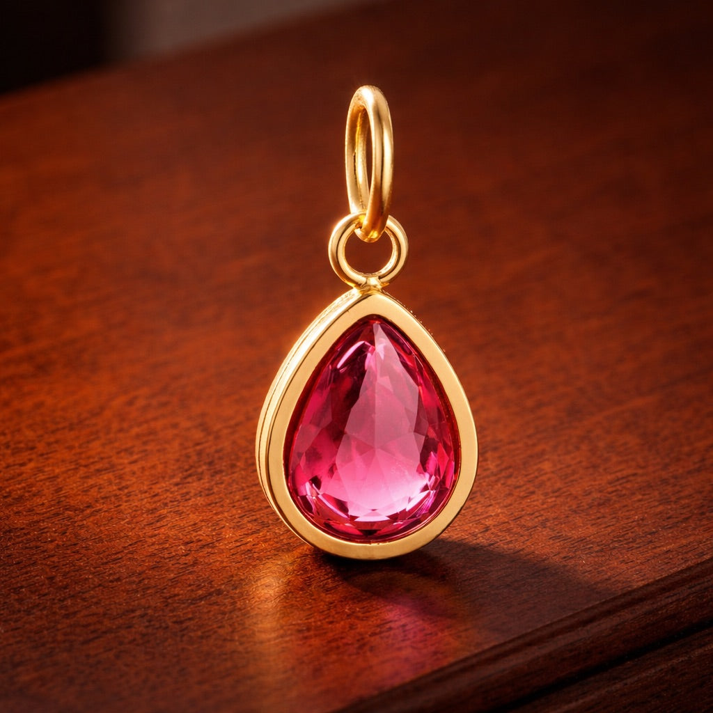 Gold pendant with a pink teardrop-shaped gemstone on a wooden surface