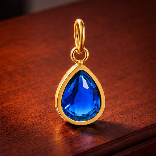 Gold pendant with a blue teardrop-shaped gemstone on a wooden surface