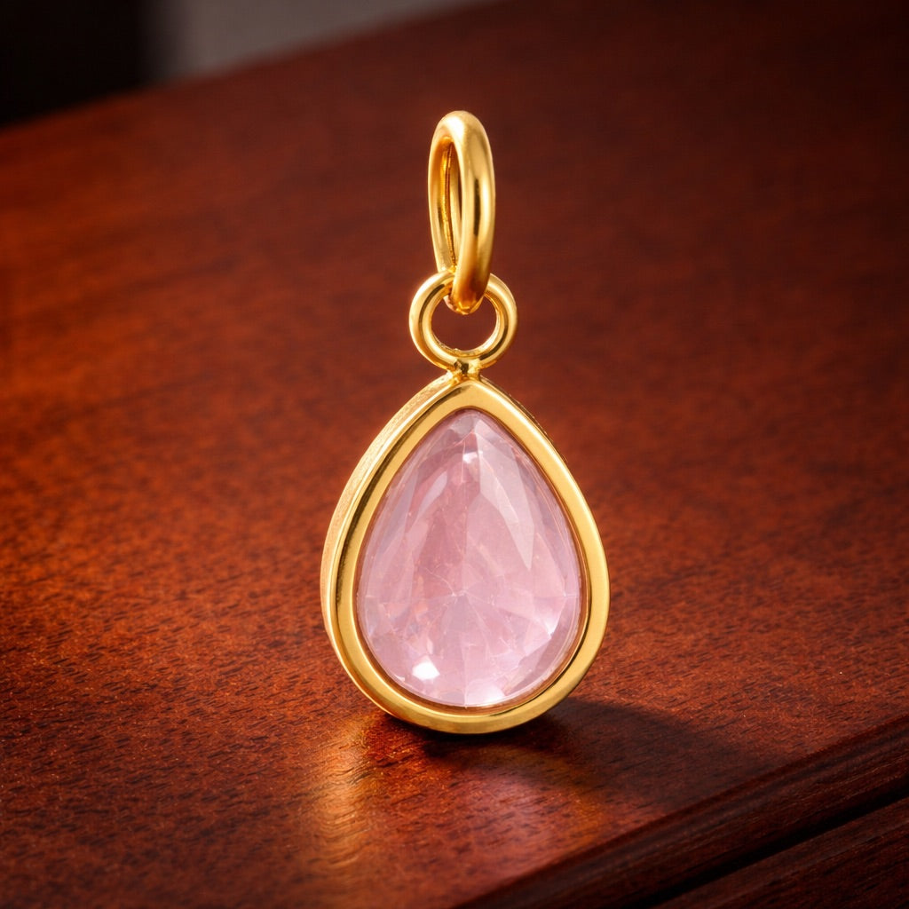Gold pendant with a pink teardrop-shaped gemstone on a wooden surface
