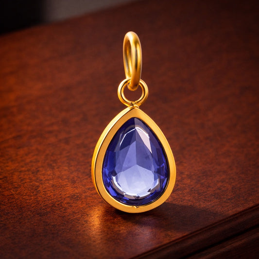 Gold pendant with a blue teardrop-shaped gemstone on a wooden surface